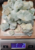 Raw Aquamarine on a digital scale showing 1kg 2g with a quarter to show size comparison.