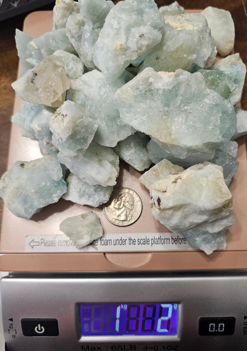 Raw Aquamarine on a digital scale showing 1kg 2g with a quarter to show size comparison.